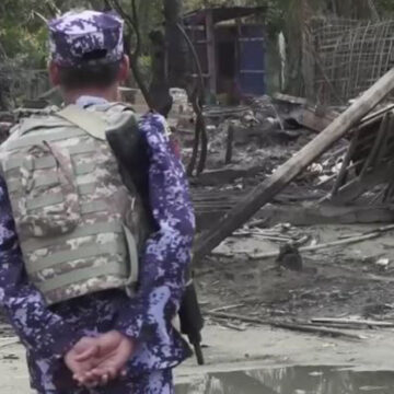 cc Steve Sandford (VOA), modified, https://commons.wikimedia.org/w/index.php?limit=500&offset=0&profile=default&search=myanmar+conflict&title=Special:Search&ns0=1&ns6=1&ns12=1&ns14=1&ns100=1&ns106=1#/media/File:BGP_officer_near_a_burnt_down_house_in_Rakhine_State.jpg