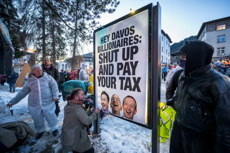 En banderoll med porträtt av Elon Musk, Jeff Bezos och Mark Zuckerberg med en slogan ses under en demonstration mot World Economic Forum (WEF) på tröskeln till WEF:s årsmöte i Davos den 18 januari 2026. (Foto av Fabrice COFFRINI / AFP)
