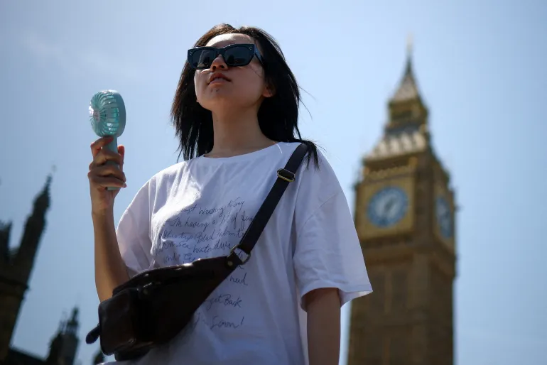En kvinna använder en fläkt när hon går nära Houses of Parliament, mitt i varmt väder i London, Storbritannien, den 23 juni 2026. REUTERS/Guglielmo Mangiapane TPX DAGENS BILDER