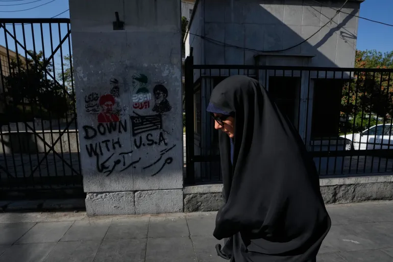 En kvinna går förbi anti-amerikansk graffiti och bilder som föreställer den bortgångne iranske högste ledaren Ayatollah Ali Khamenei målade på en vägg längs gatan Islamic Revolution i centrala Teheran, Iran, lördagen den 29 augusti 2026. (AP Photo/Vahid Salemi)