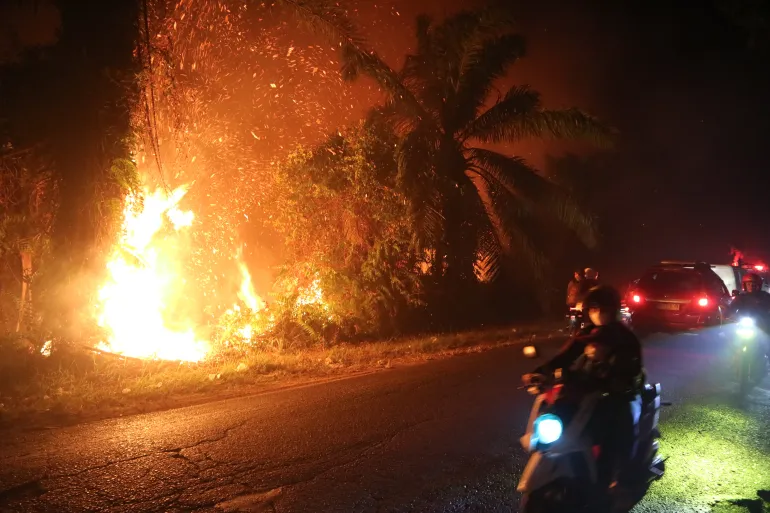 Bilister åker förbi en löpeld som brinner genom en torvmark i Sampit, centrala Kalimantan, Indonesien, den 24 augusti 2026