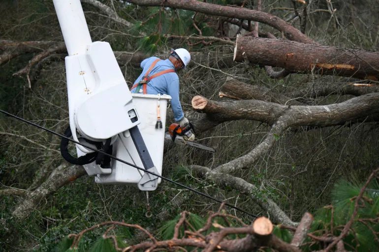 Florida Power & Light-arbetaren Yosvany Quintero rensar ner nedfällda trädgrenar orsakade av effekterna av Isaias lördagen den 10 oktober 2026 i East Milton, Florida (AP Photo/Octavio Jones)
