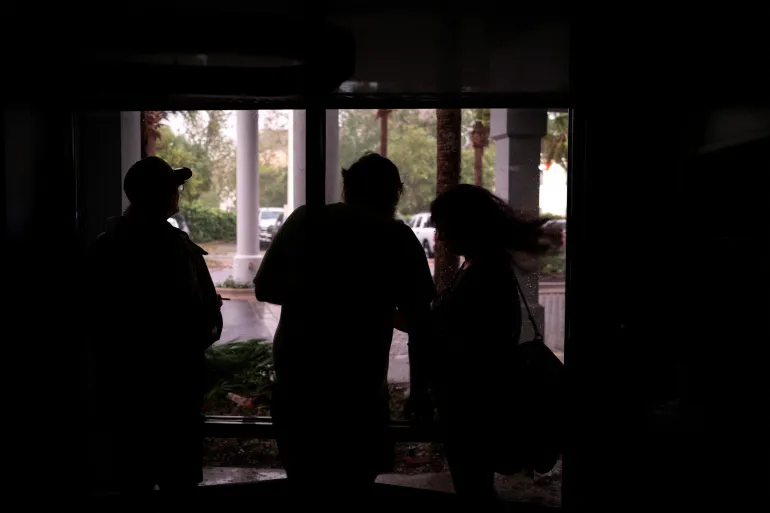 Människor tittar på vind, regn och flygande skräp från en hotellobby under ett strömavbrott inför ankomsten av orkanen Isaias, i Pensacola, Florida, USA, den 9 oktober 2026. REUTERS/Marco Bello