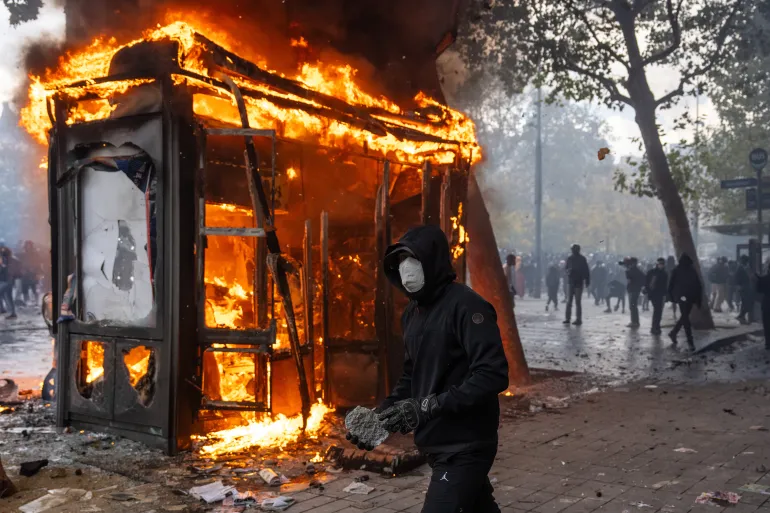 PARIS, FRANKRIKE - 17 OKTOBER: En demonstrant håller en sten för att kasta mot polisen när en kiosk brinner under en demonstration nära Place de la République, när Gilets Jaunes går med studenter för en helg av action den 17 oktober 2026 i Paris, Frankrike. Gilets Jaunes (gula västar) engagemang i de pågående franska skolblockaderna utökar omfattningen av dessa demonstrationer genom att koppla lokala elevers klagomål till en bredare ekonomisk politik. Studentkårer initierade ursprungligen rörelsen för att protestera mot underfinansiering, försämrad infrastruktur och akut lärarbrist på franska gymnasieskolor och universitet. Genom att gå med i protesterna introducerar Gilets Jaunes sin etablerade plattform mot åtstramningsnedskärningar, stigande levnadskostnader och stigande bränslepriser i den ungdomsledda aktionen. (Foto av Carl Court/Getty Images)